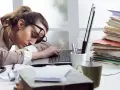 Zmęczona kobieta śpi na laptopie, otoczona stertami dokumentów. To obrazek pokazujący skutki związku z pracoholikiem.