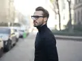 Elegancki mężczyzna w czarnym golfie i okularach, zamyślony, jakby planował zagrywki zakochanego faceta.