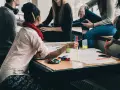 Grupa młodych ludzi przy stole, dyskutująca i tworząca coś na papierze. Uczą się, jak rozmawiać z ludźmi, wymieniając się pomysłami.