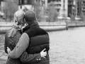 Para przytulająca się nad wodą. Jej ręka obejmuje jego talię, a jego ramiona otulają ją. Delikatny dotyk w relacjach damsko-męskich.