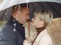 Para w deszczu pod parasolem. Młodszy partner patrzy z czułością na swoją ukochaną.
