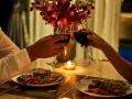 Para romantyczna kolacja: para wznosi toast winem przy świecach, z pięknymi kwiatami i pysznym jedzeniem.