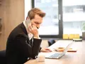 Mężczyzna w garniturze prowadzi ważną rozmowę przez telefon, siedząc przy biurku z laptopem i filiżanką kawy.