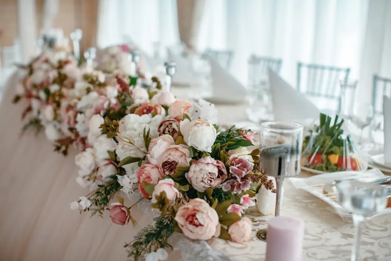 Elegancki wystrój sali weselnej z obfitymi bukietami piwonii w pastelowych kolorach, tworzącymi romantyczną atmosferę.