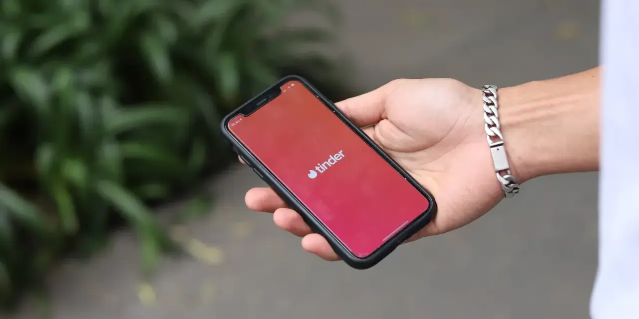 Dłoń trzyma smartfon z logo Tinder. Zastanawiasz się, czy Tinder jest płatny? Aplikacja oferuje darmowe funkcje, ale płatne subskrypcje dają więcej możliwości.