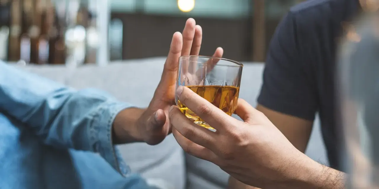 Dłoń odrzuca szklankę z alkoholem. Przykład asertywnego odmawiania picia alkoholu.