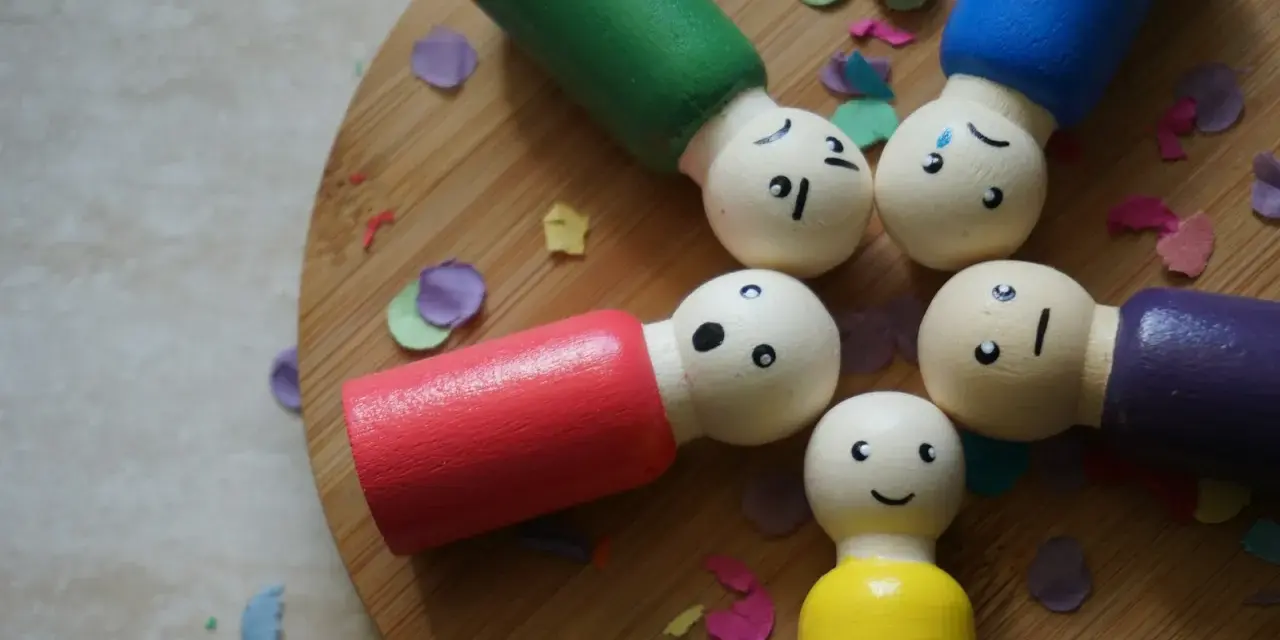 Drewniane ludziki z różnymi minami, otoczone konfetti, symbolizują niestabilność emocjonalną w związku.
