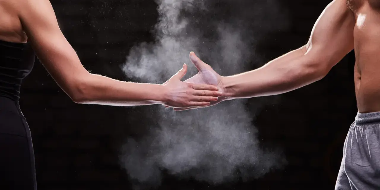 Dwie dłonie, męska i kobieca, spotykają się w chmurze magnezji. Pokazuje to siłę i determinację, cechy, które mogą być obecne u każdego, niezależnie od płci.
