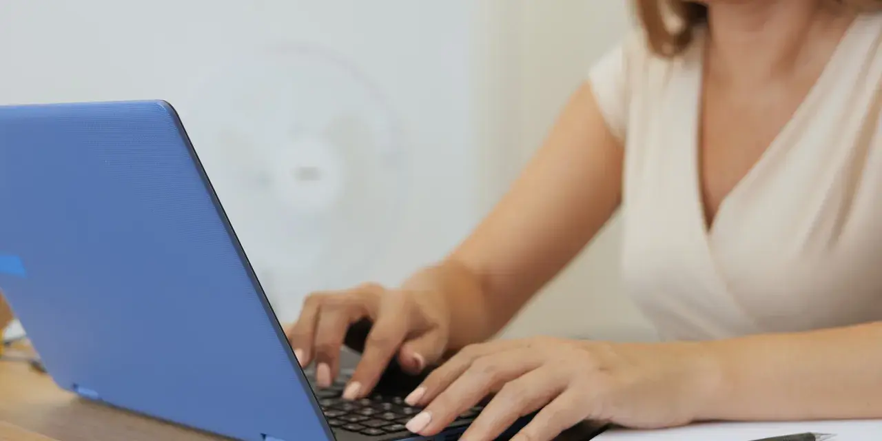 Kobieta pisze na laptopie, tworząc idealny profil. Zastanawiasz się, jakie rzeczy o których kłamiemy na portalach randkowych ukrywa?