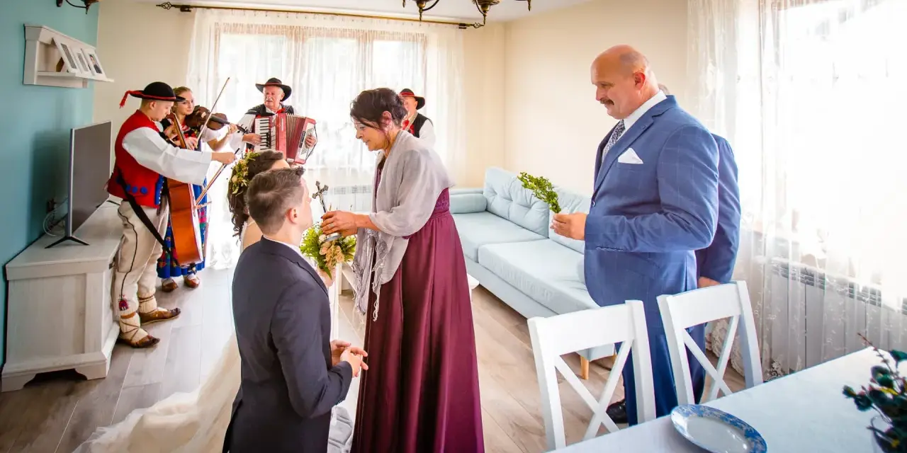 Wzruszający moment błogosławieństwa matki chrzestnej dla narzeczonego. W tle grają górale.