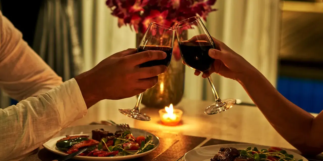 Para wznosząca toast kieliszkami z czerwonym winem podczas romantycznej kolacji przy świecach.