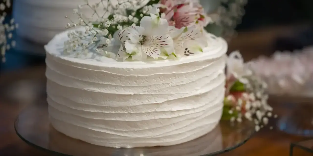 Elegancki tort weselny z żywymi kwiatami, udekorowany delikatnymi białymi kwiatami i gipsówką.