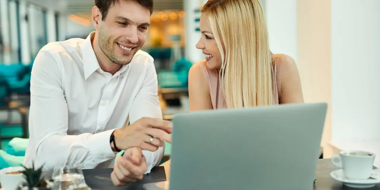 Uśmiechnięci współpracownicy przy laptopie. Ich spojrzenia i gesty sugerują, że to nie tylko praca, ale i rodząca się miłość w pracy.