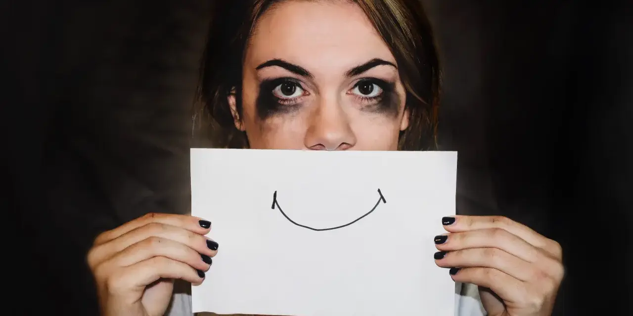 Dziewczyna z rozmazanym makijażem ukrywa usta za kartką z uśmiechem. Trudna samoregulacja emocji.