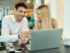 Uśmiechnięci współpracownicy przy laptopie. Ich spojrzenia i gesty sugerują, że to nie tylko praca, ale i rodząca się miłość w pracy.