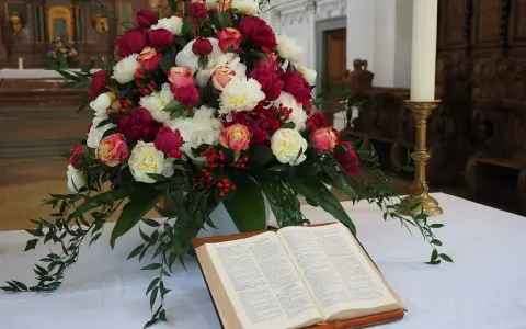 Piękne kwiaty pod ołtarz na ślub: bukiet różowych i białych piwonii, różyczek i czerwonych jagódek, obok otwarta księga.