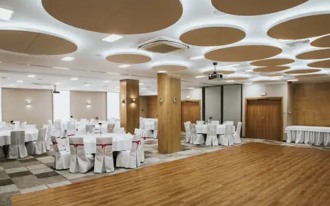 Elegancka sala bankietowa gotowa na wesele we wrześniu. Okrągłe stoły z białymi pokrowcami i czerwonymi wstążkami czekają na gości.