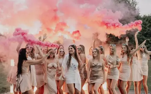 Grupa kobiet świętuje wieczór panieński, otoczona różowym dymem. Kto płaci za panienski? Dziewczyny bawią się świetnie!