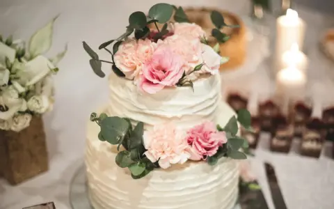 Elegancki tort weselny z kremową dekoracją i pastelowymi kwiatami, ozdobiony gałązkami eukaliptusa.