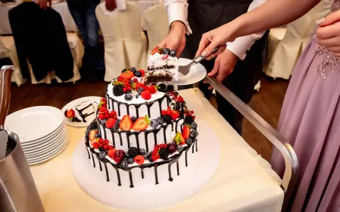 Piękne torty weselne z owocami, ozdobione czekoladą i świeżymi jagodami, malinami i truskawkami. Para kroi pierwszy kawałek.