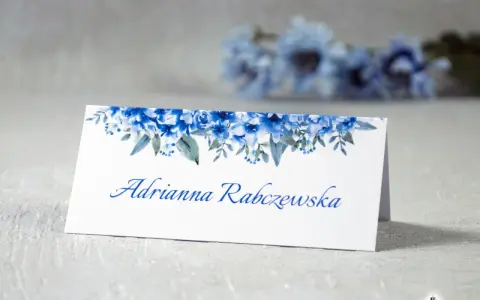 Eleganckie winietki dla usługodawców z motywem niebieskich kwiatów. Na białej kartce widnieje imię i nazwisko "Adrianna Rabczewska".