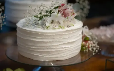 Elegancki tort weselny z żywymi kwiatami, udekorowany delikatnymi białymi kwiatami i gipsówką.