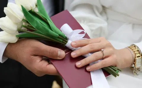 Para weselna trzyma bukiet białych tulipanów i akt małżeństwa. Zastanawiasz się, ile się daje na wesele?