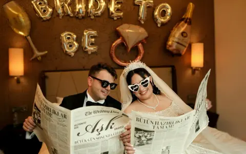 Para Młoda czyta gazetę z nagłówkiem "przykładowy harmonogram wesela". Balony "Bride to be" i kieliszek szampana w tle.