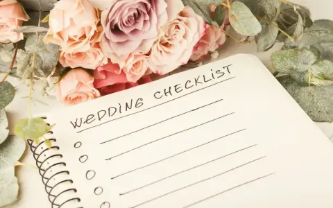 Bukiet róż i eukaliptusa obok notatnika z napisem "Wedding Checklist". Planowanie przebiegu wesela zaczyna się od listy zadań.
