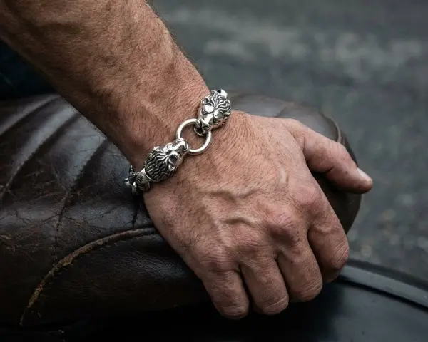 Męska dłoń z bransoletą z lwimi głowami, symbolizującą gest, kiedy mężczyzna daje kobiecie biżuterię.