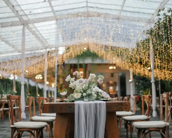 Eleganckie wesele pod baldachimem z tysiącami światełek. Stół z bukietem kwiatów i zwiewnym materiałem zaprasza do świętowania.