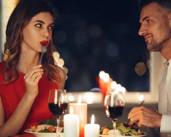 Romantyczna kolacja przy świecach. Ona, w czerwonej sukience, zmysłowo je, a on patrzy na nią z uwielbieniem. Widać oznaki flirtu dziewczyny w jej spojrzeniu.