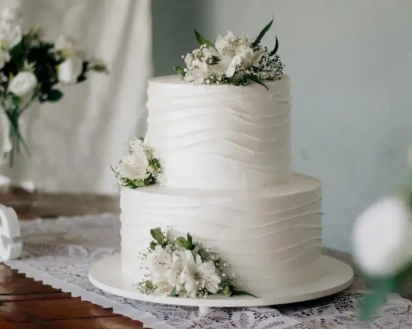 Elegancki tort weselny z białymi kwiatami, idealny na życzenia na ślub dla przyjaciół.