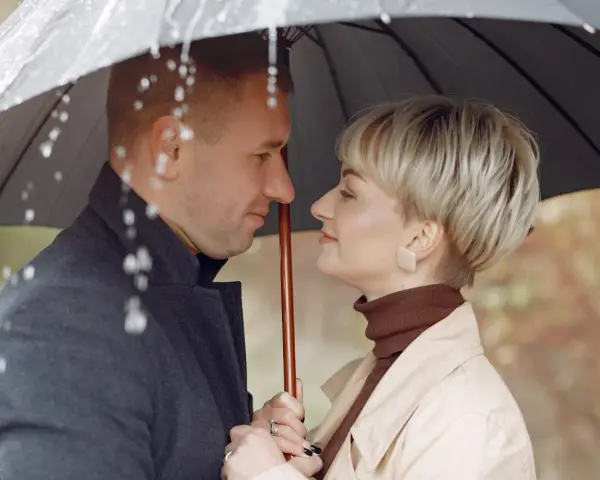 Para w deszczu pod parasolem. Młodszy partner patrzy z czułością na swoją ukochaną.