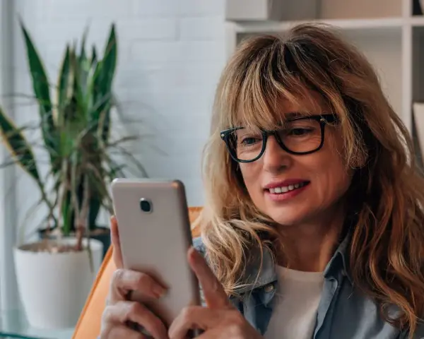Kobieta w okularach przegląda telefon, być może szuka bratniej duszy na **Bumble w Polsce**.