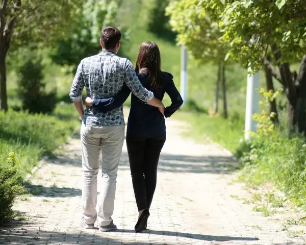 Para niego romantyczne gesty to spacer z objęciem. Para idzie alejką w parku, otoczona zielenią.