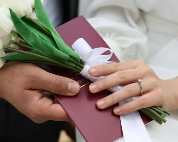 Para weselna trzyma bukiet białych tulipanów i akt małżeństwa. Zastanawiasz się, ile się daje na wesele?