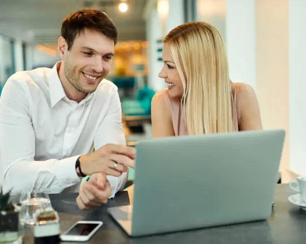 Uśmiechnięci współpracownicy przy laptopie. Ich spojrzenia i gesty sugerują, że to nie tylko praca, ale i rodząca się miłość w pracy.