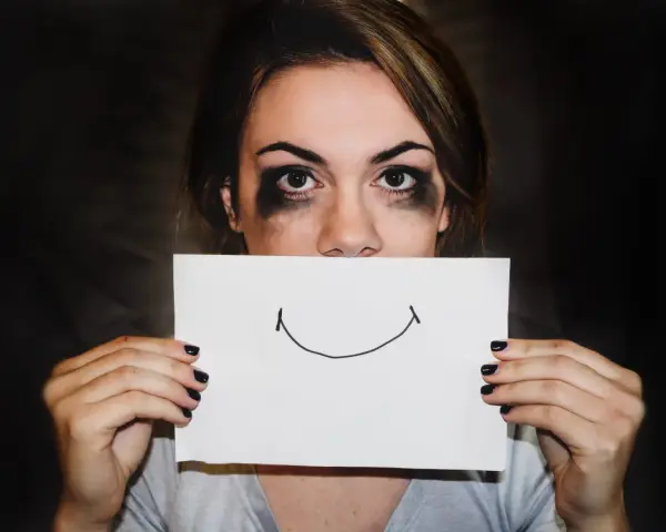 Dziewczyna z rozmazanym makijażem ukrywa usta za kartką z uśmiechem. Trudna samoregulacja emocji.