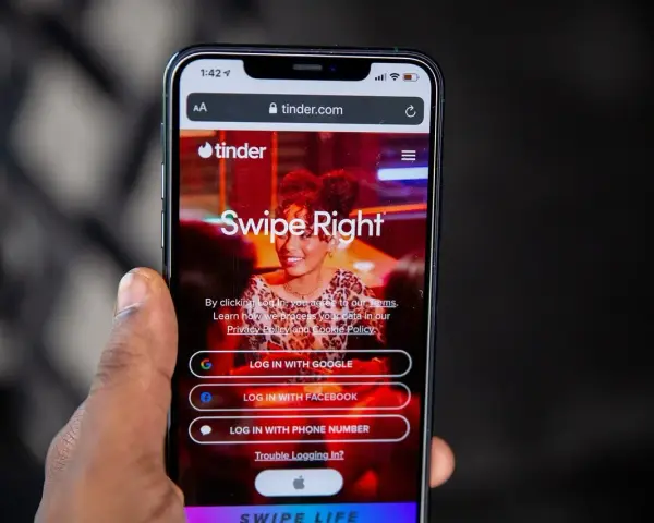 Telefon z aplikacją Tinder. Widoczne opcje logowania: Google, Facebook, numer telefonu. Czas na skróty na Tinderze!