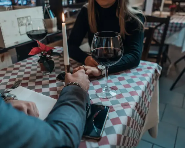 Romantyczna kolacja, świeca, wino i dłonie splecione na stole. Widać, jak angażuje się mężczyzna, skupiony na partnerce.