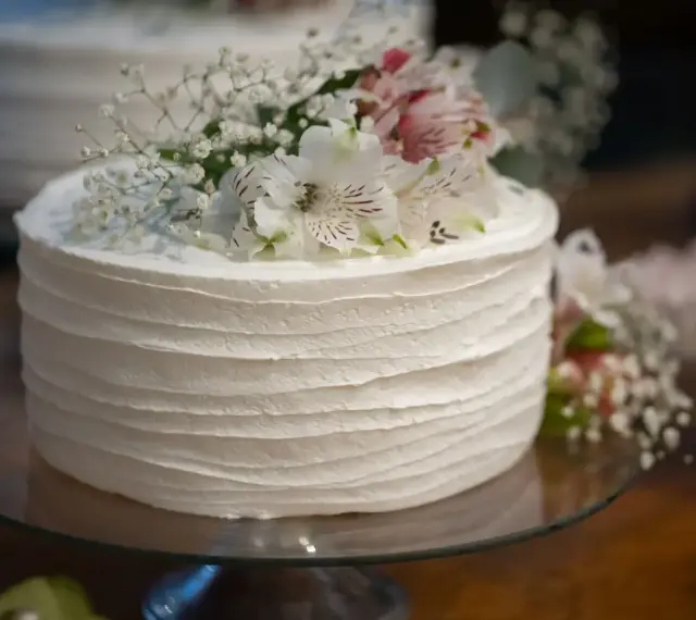 Elegancki tort weselny z żywymi kwiatami, udekorowany delikatnymi białymi kwiatami i gipsówką.