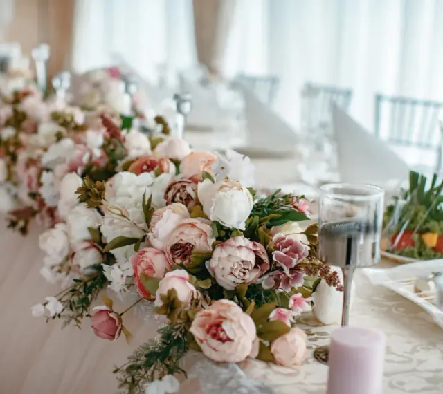 Elegancki wystrój sali weselnej z obfitymi bukietami piwonii w pastelowych kolorach, tworzącymi romantyczną atmosferę.
