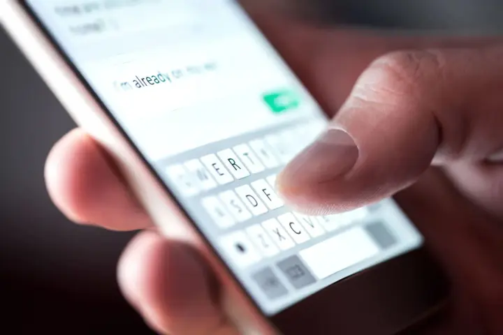 Palec pisze na klawiaturze telefonu: "Już w drodze na wesele!". Potwierdzenie przybycia na wesele sms.
