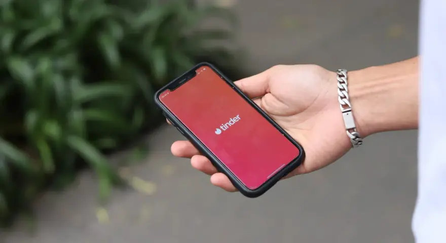 Dłoń trzyma smartfon z logo Tinder. Zastanawiasz się, czy Tinder jest płatny? Aplikacja oferuje darmowe funkcje, ale płatne subskrypcje dają więcej możliwości.