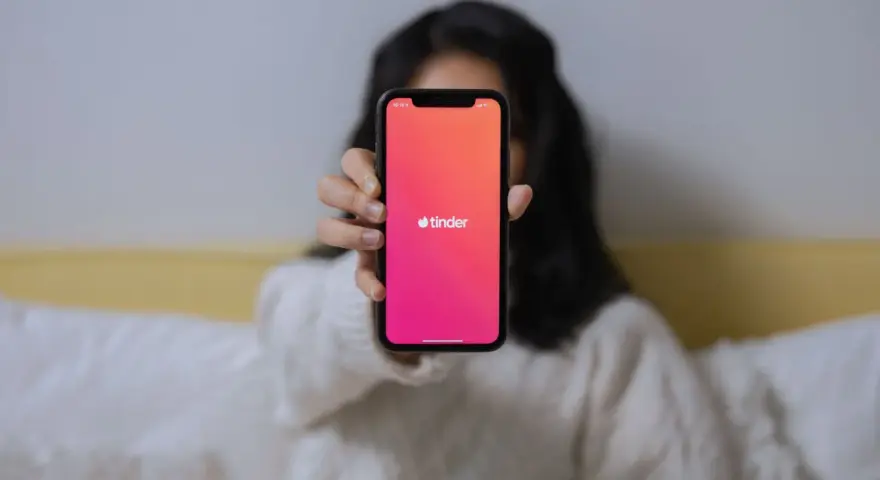 Osoba trzyma telefon z widocznym logo Tindera. Chcesz wiedzieć, jak sprawdzić, czy ktoś ma Tindera?