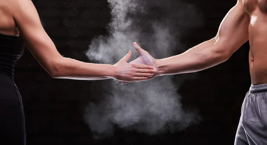 Dwie dłonie, męska i kobieca, spotykają się w chmurze magnezji. Pokazuje to siłę i determinację, cechy, które mogą być obecne u każdego, niezależnie od płci.