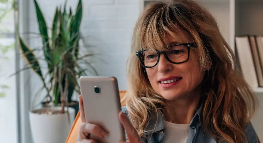 Kobieta w okularach przegląda telefon, być może szuka bratniej duszy na **Bumble w Polsce**.