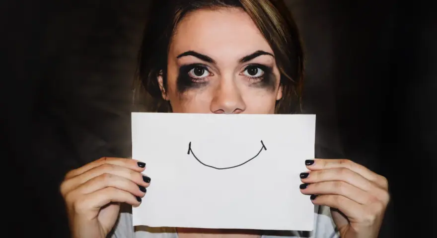 Dziewczyna z rozmazanym makijażem ukrywa usta za kartką z uśmiechem. Trudna samoregulacja emocji.