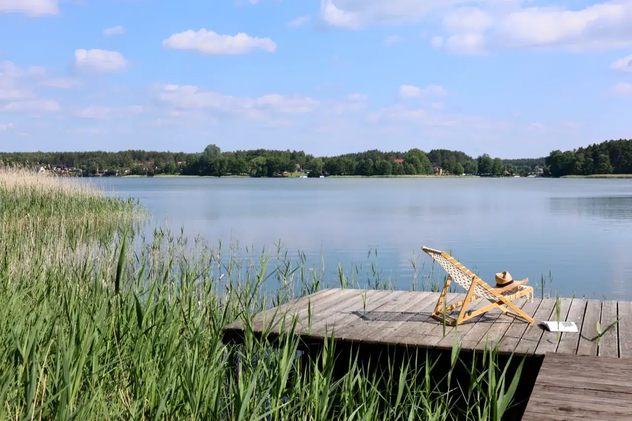Idealne romantyczne miejsce na Kaszubach: drewniany pomost nad jeziorem, leżak, słomkowy kapelusz i książka.